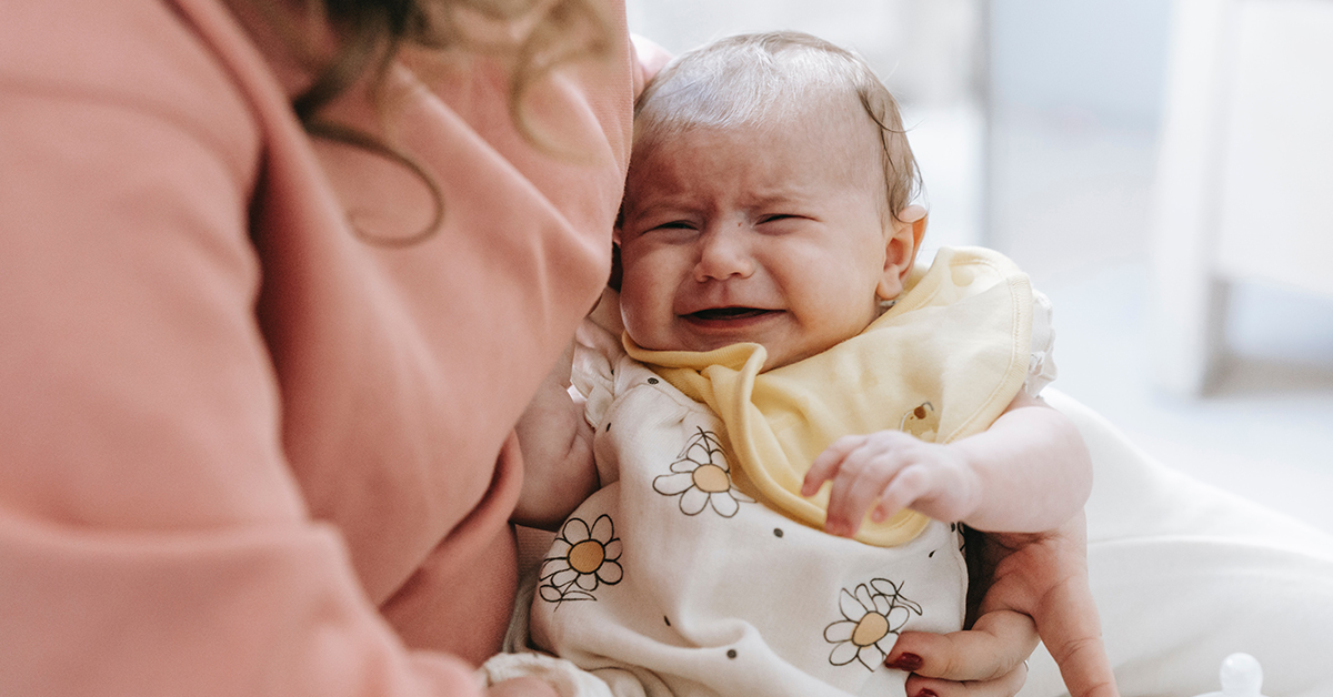 a cranky baby cries while being held by mother