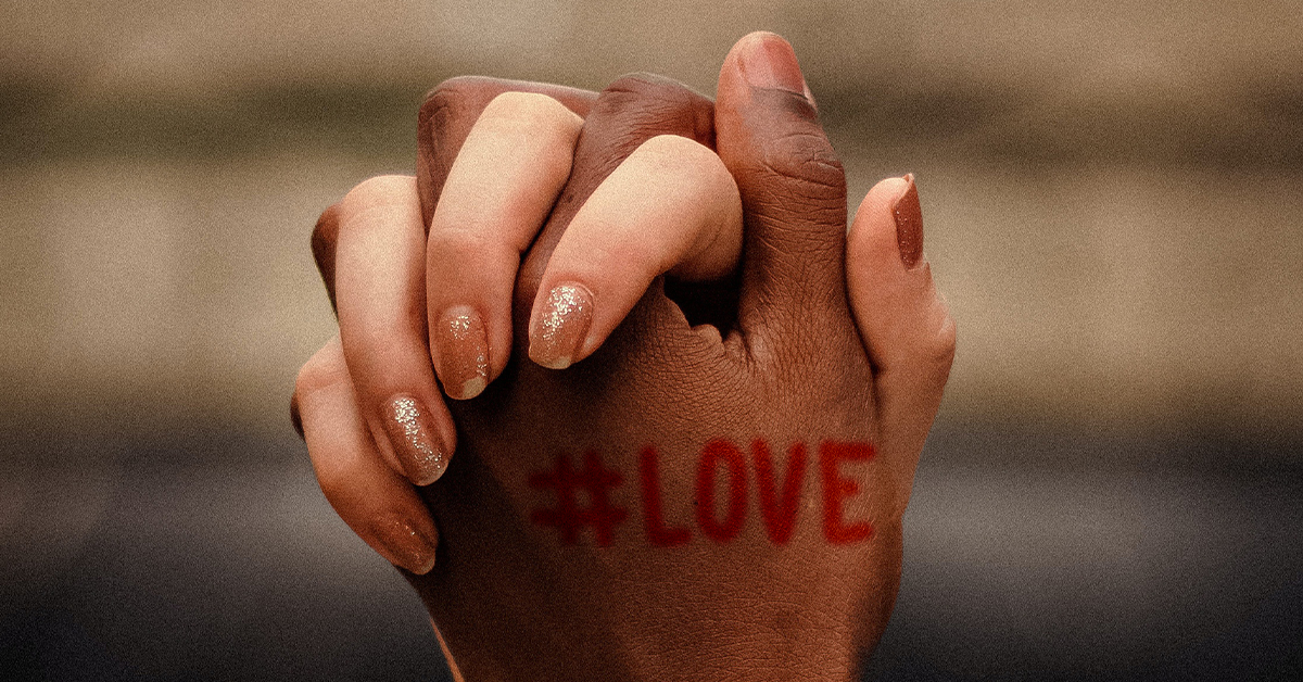 Close up of couple holding hands with #LOVE written on one of the hands