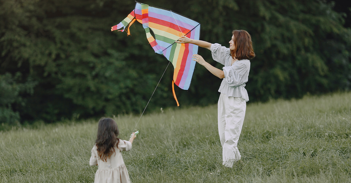 A mom and her daughter play with a rainbow kite in the field