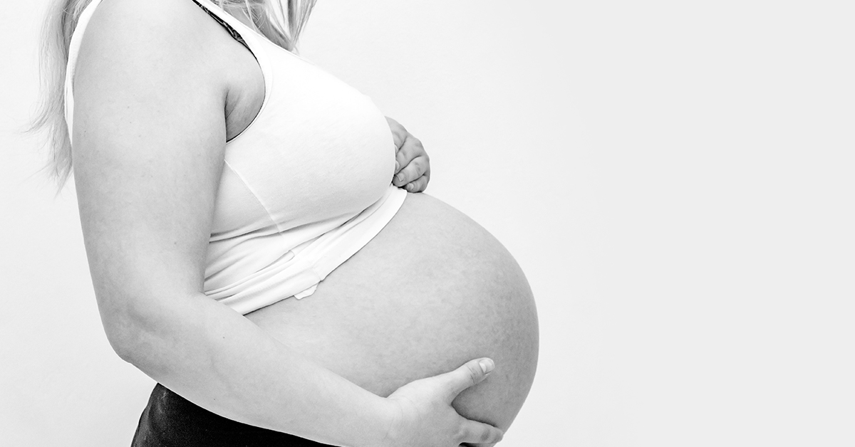 Side profile image of a woman holding her pregnant belly