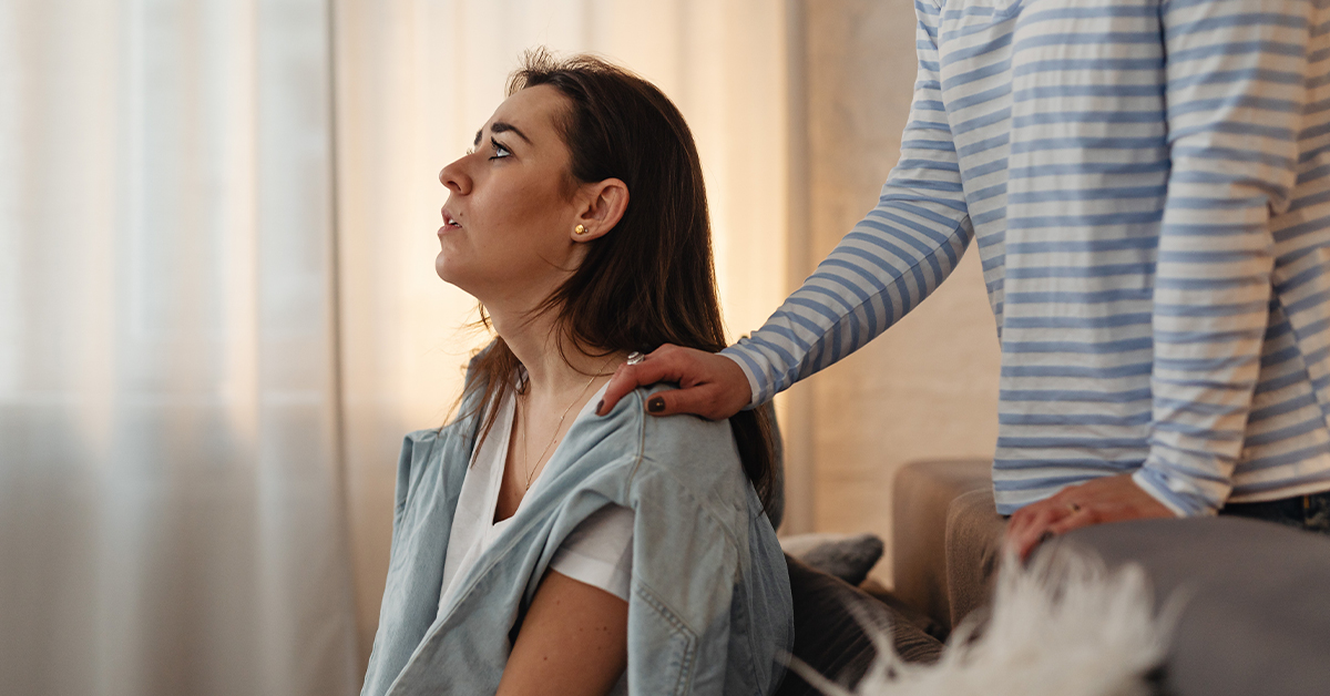 Exhausted woman receives comforting hand on shoulder from another woman.